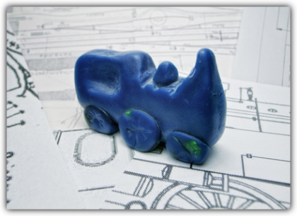 The image depicts a blue locomotive model made from modeling clay on a locomotive blueprint. When you hover over the picture, a brief description appears: Design - Develop alternative concepts for implementing the goals during the concept development phase and select the most suitable concept.<br />©memephoto