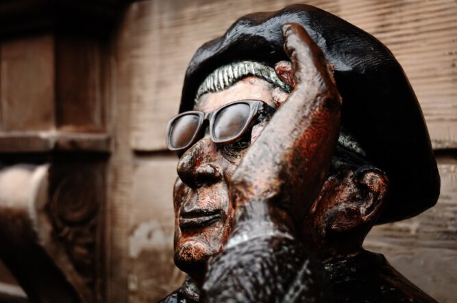 The photo shows a detail of a statue in Stockholm. It shows a man with a hat lifting his sunglasses to look underneath them.<br />©memephoto