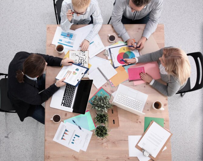The photo shows four people working at a table covered with papers, taken from a bird's-eye view.<br />©Stocknation