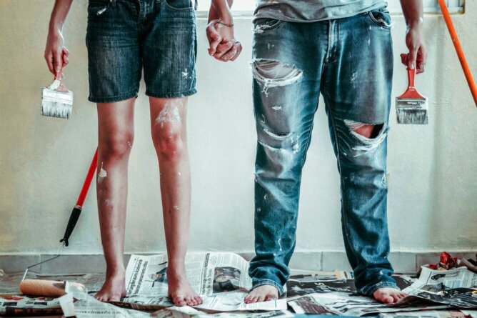 The photo shows the lower half of a man and a woman in painters' overalls, each holding a paintbrush. <br />©Stocknation