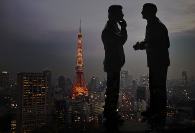 The photo shows two men conversing in a skyscraper overlooking the Tokyo skyline.<br />©memephoto