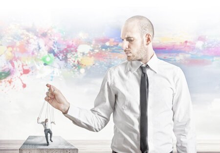 Puppeteer A man in a white shirt and tie holds strings in his right hand to control a marionette.<br />©alphaspirit